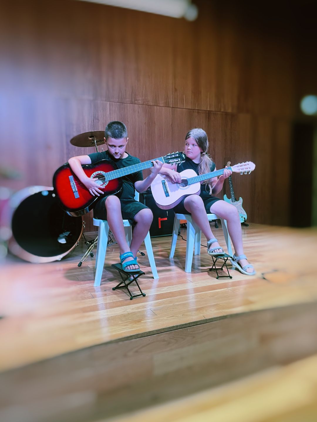 Two beginner students performing classical guitar on the wooden stage at La Violeta in Gracia, Barcelona, at a Shine Music School beginners concert